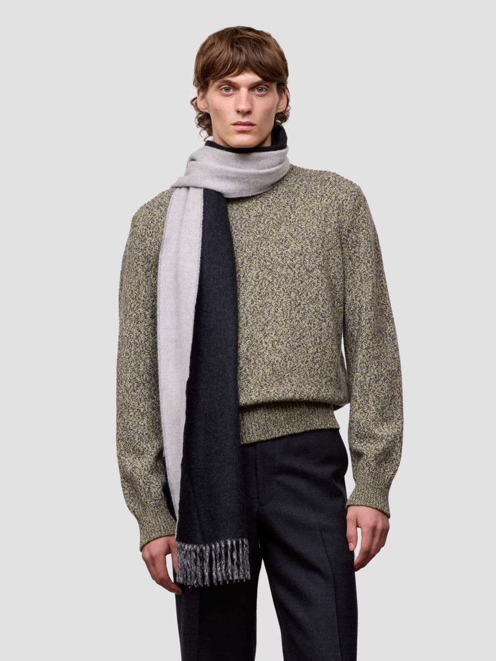 Man wearing a patterned sweater and scarf on a plain background