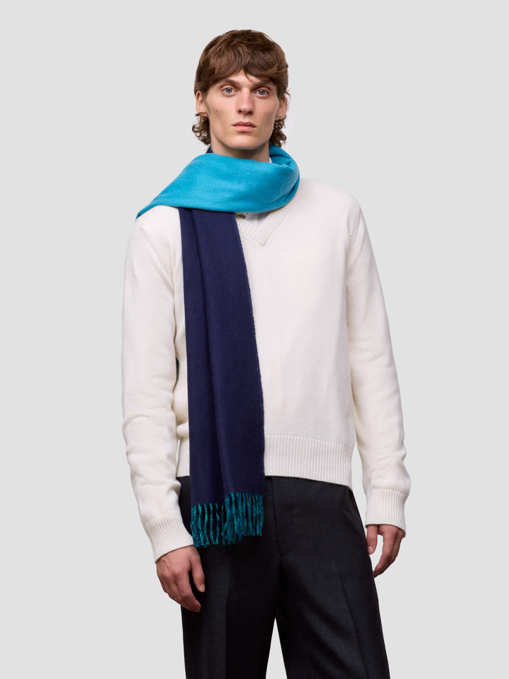 Man wearing a white sweater and colorful reversible blue scarf on a light gray background
