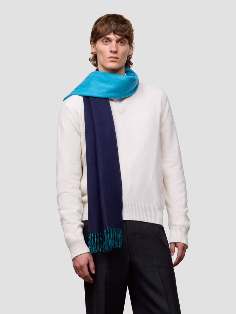 Man wearing a white sweater and colorful reversible blue scarf on a light gray background
