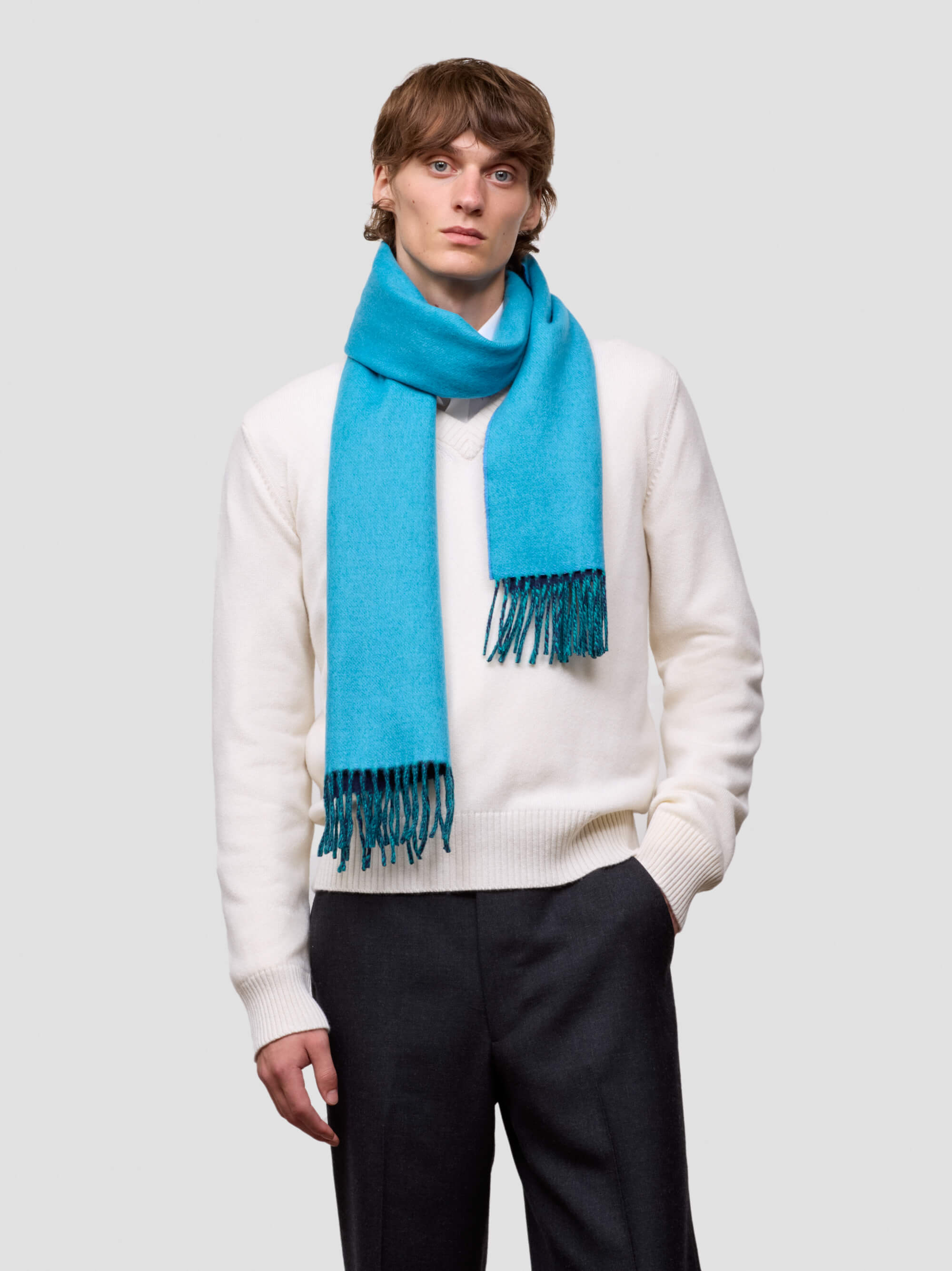 Man wearing a bright blue scarf and white sweater on a light gray background