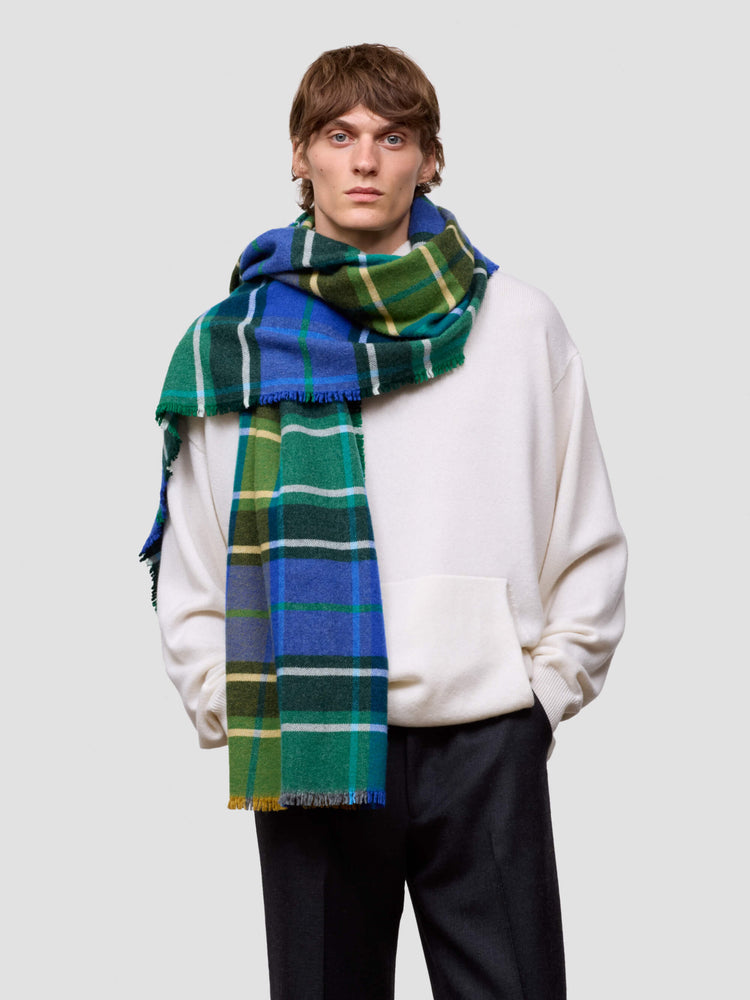 man wearing a large plaid scarf in blue, green, and white on a plain background