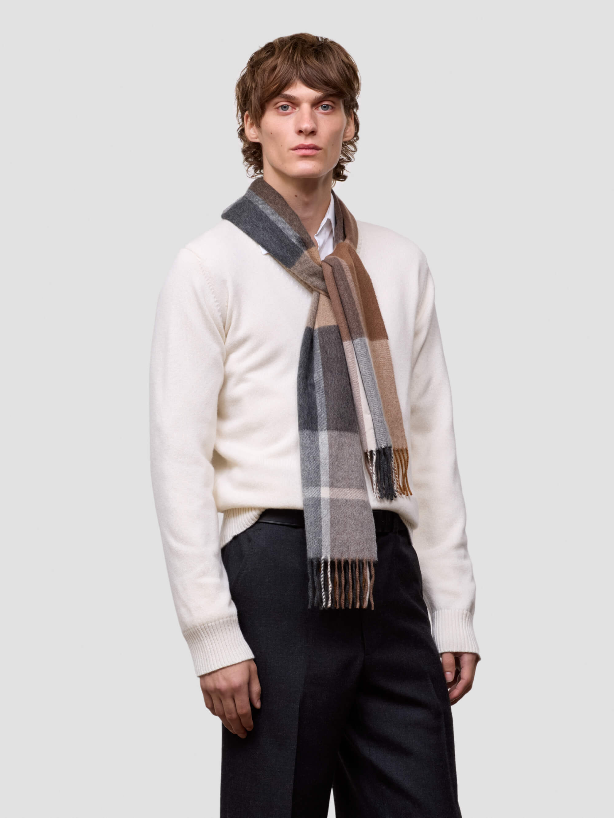 Man wearing a white sweater and plaid scarf on a light gray background