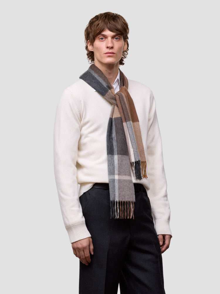 Man wearing a white sweater and plaid scarf on a light gray background