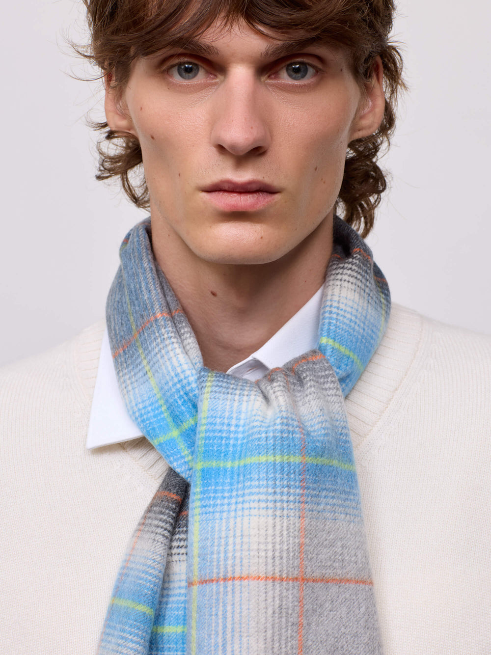 man wearing a white sweater and grey blue checked cashmere scarf on plain background