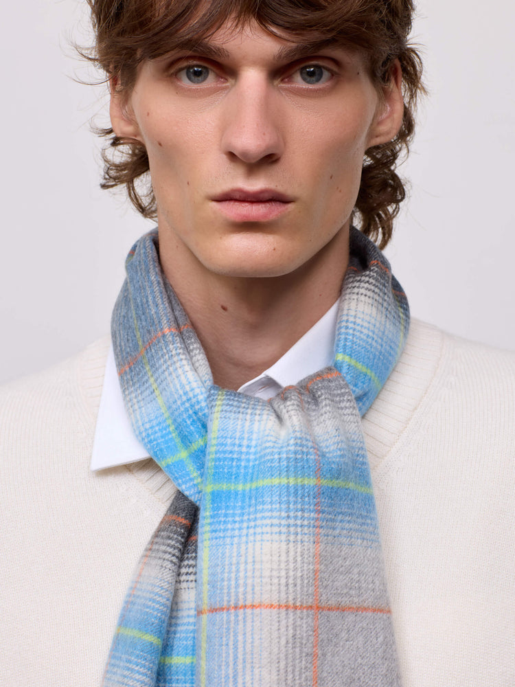 man wearing a white sweater and grey blue checked cashmere scarf on plain background