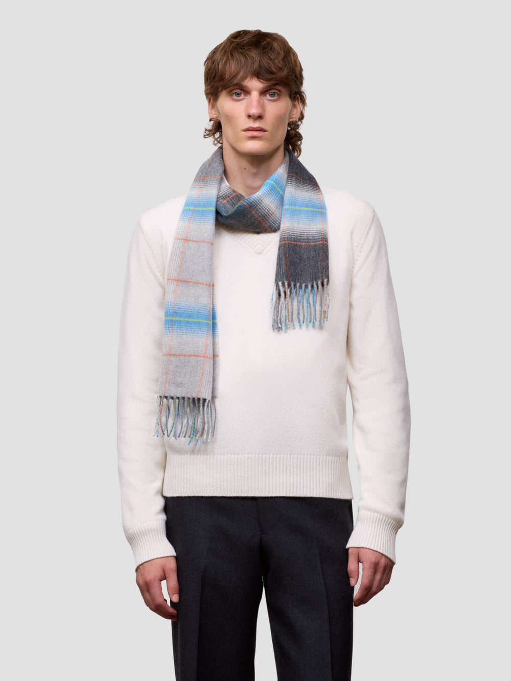 man wearing a white sweater and grey blue checked cashmere scarf on plain background