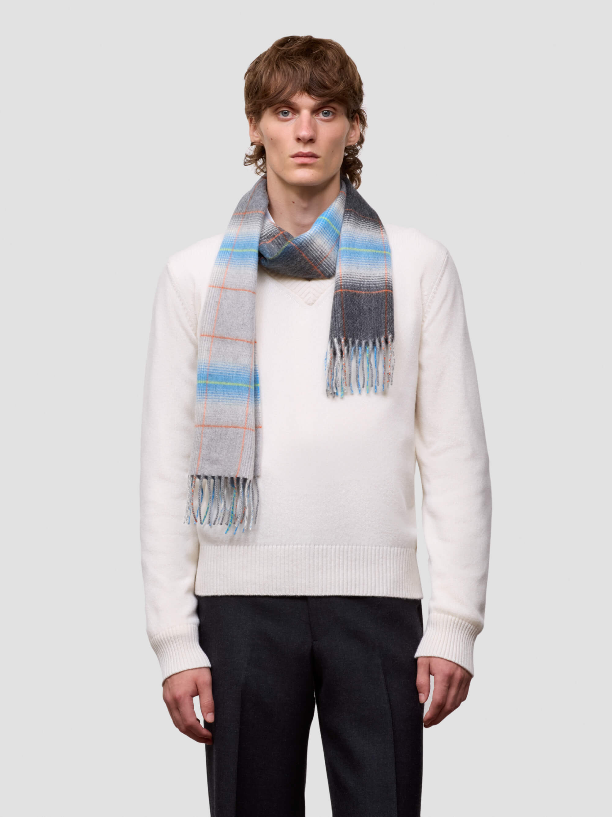 man wearing a white sweater and grey blue checked cashmere scarf on plain background