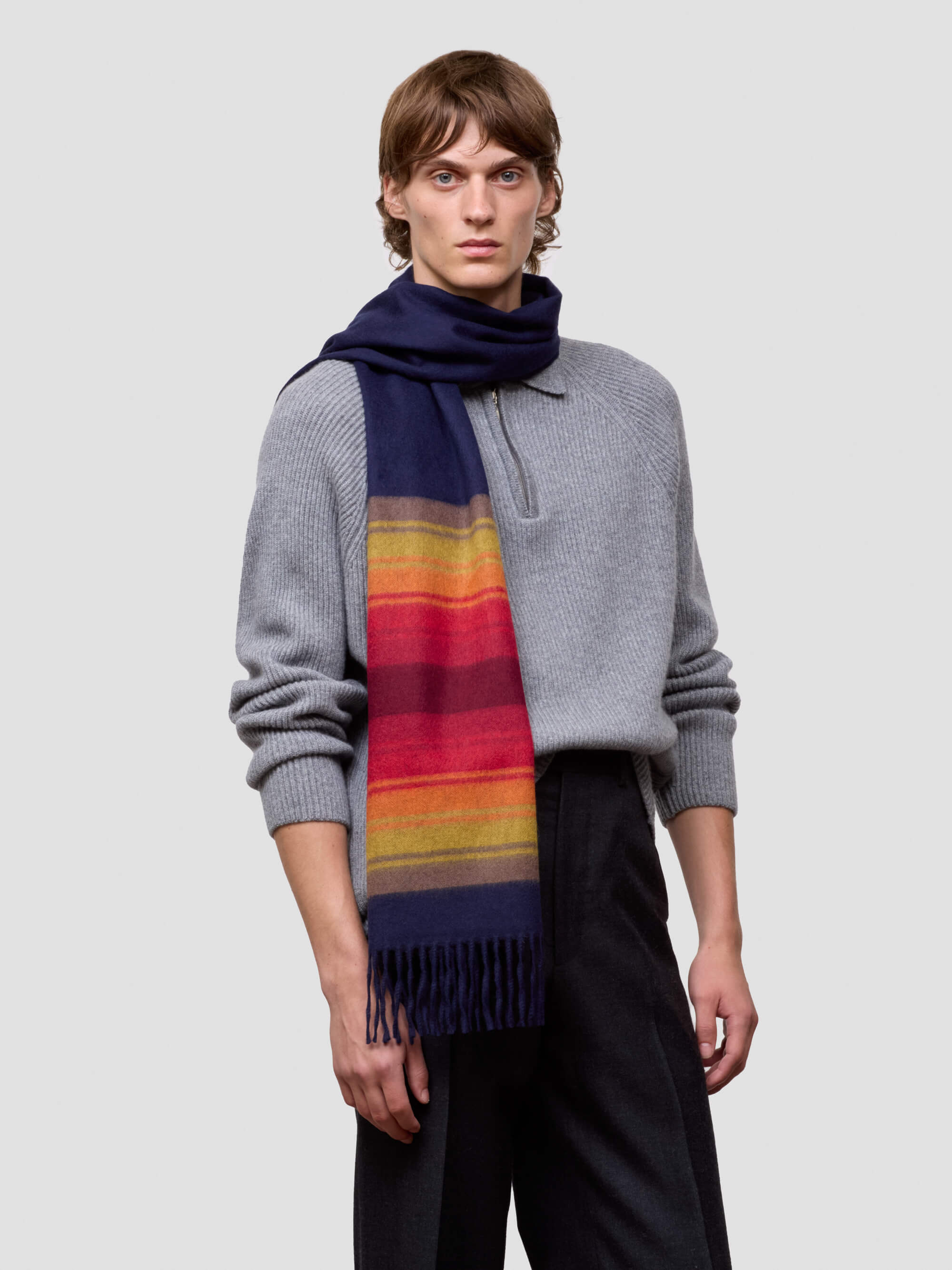 man wearing a grey zip jumper and striped navy and red cashmere scarf on plain background