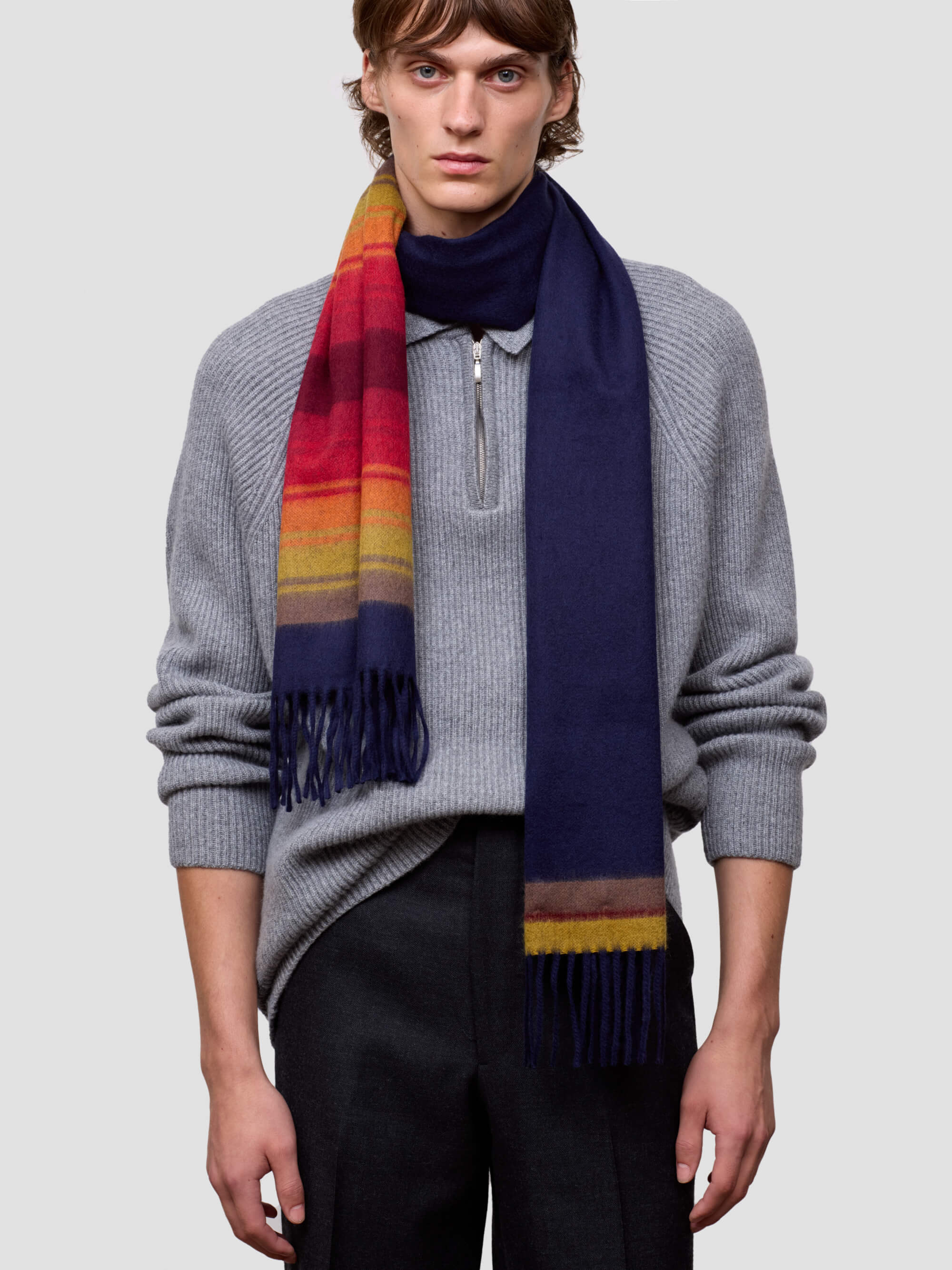 man wearing a grey zip jumper and striped navy and red cashmere scarf on plain background