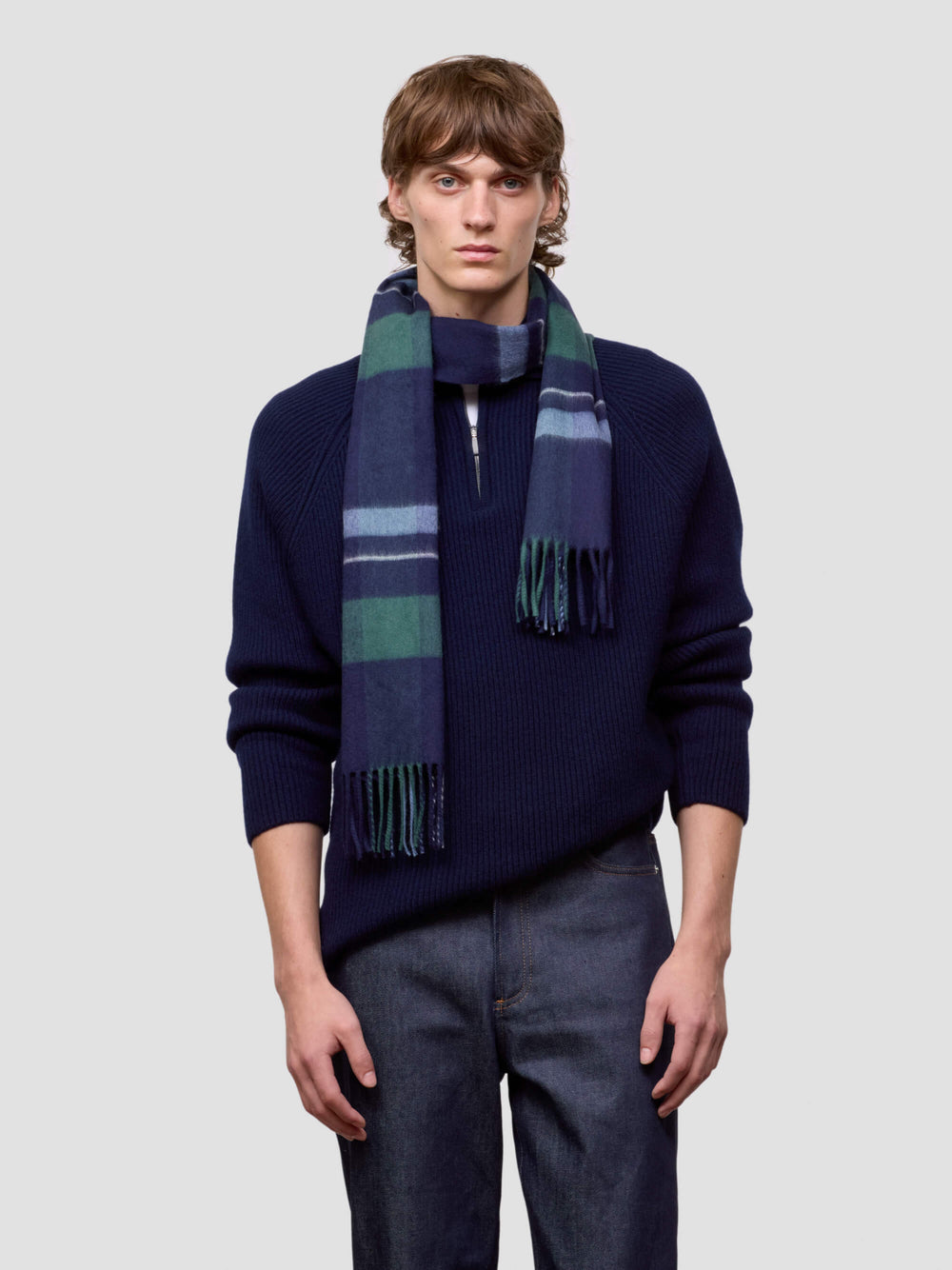 Man wearing a navy sweater and plaid scarf against a light gray background