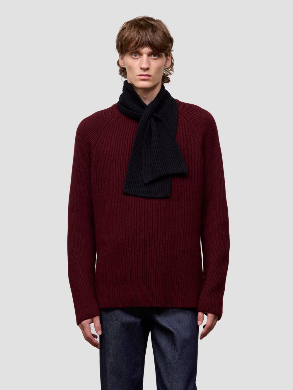 Person wearing a burgundy sweater with a black scarf on a light gray background