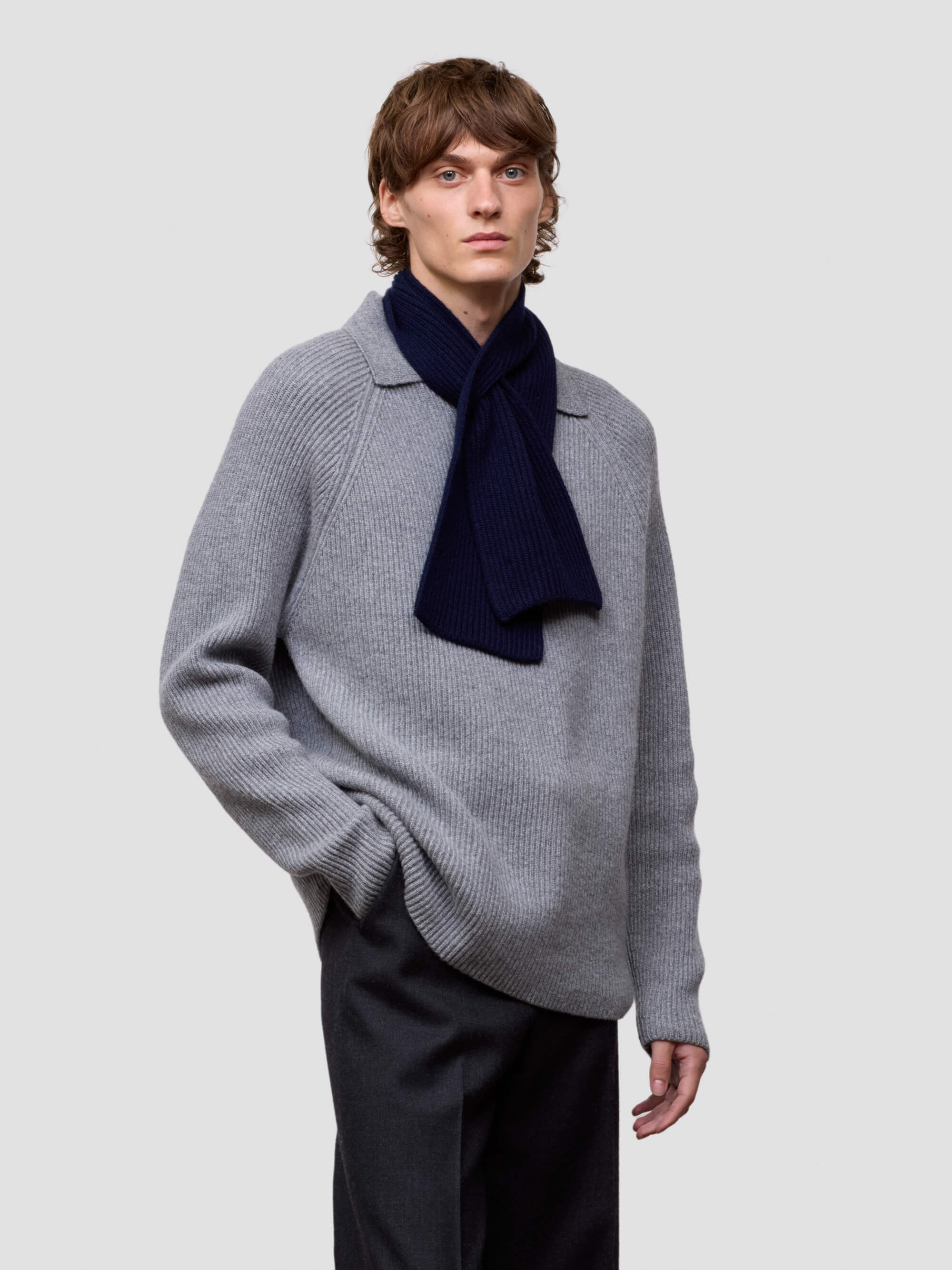 Person wearing a gray sweater with a navy scarf on a light gray background