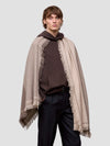 Man wearing a brown cashmere hoodie and beige scarf with fringes on a light gray background