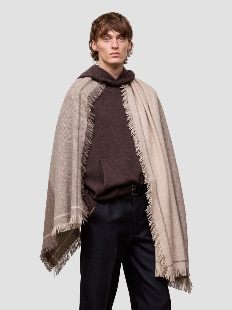Man wearing a brown cashmere hoodie and beige scarf with fringes on a light gray background