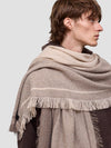man wearing a beige shawl with fringes on a plain background