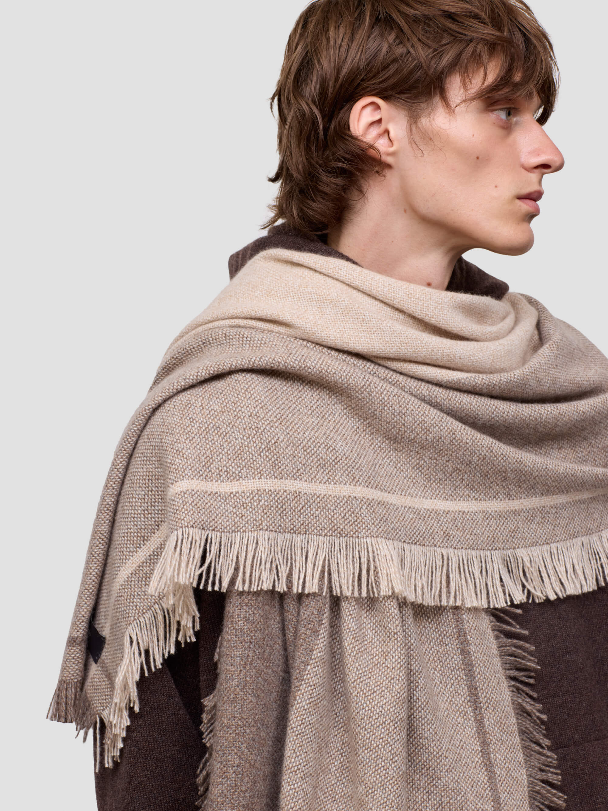 man wearing a beige shawl with fringes on a plain background