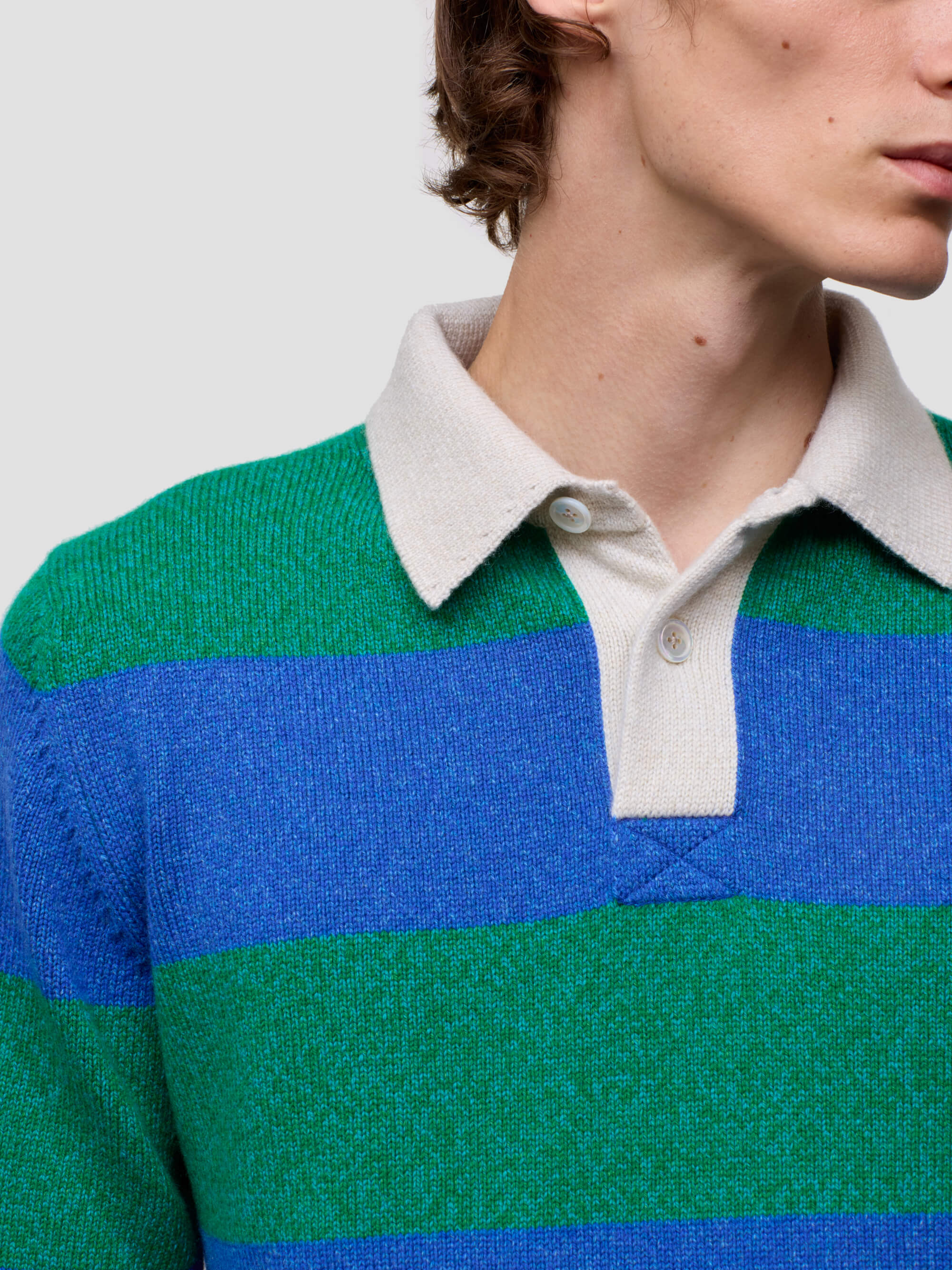 Close-up of a person wearing a green and blue striped sweater with a white collar.
