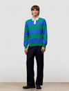 Person wearing a blue and green striped sweater with a white shirt underneath, standing against a plain background.