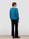 Person wearing a blue and green striped sweater with black pants on a plain background