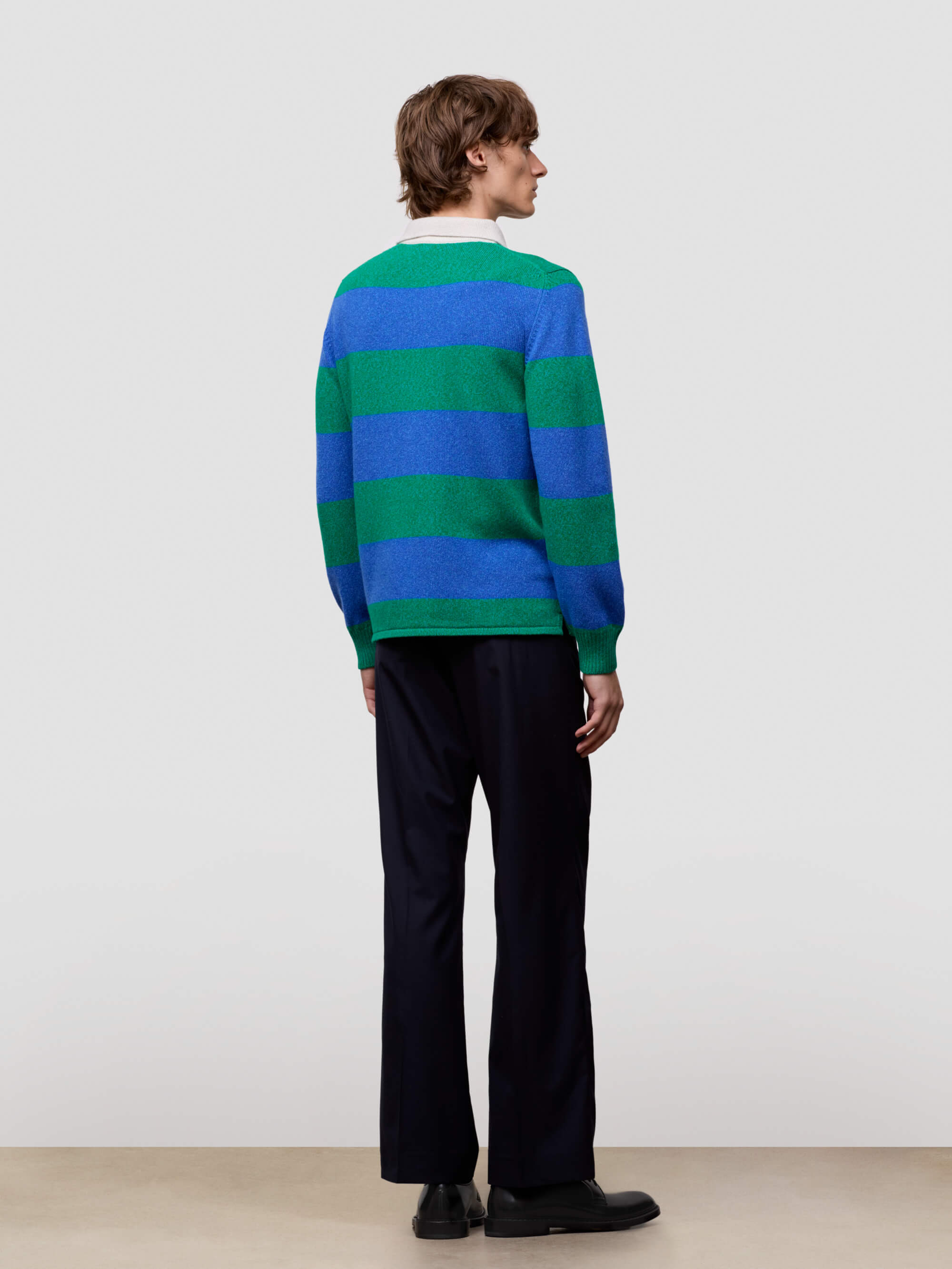 Person wearing a blue and green striped sweater with black pants on a plain background