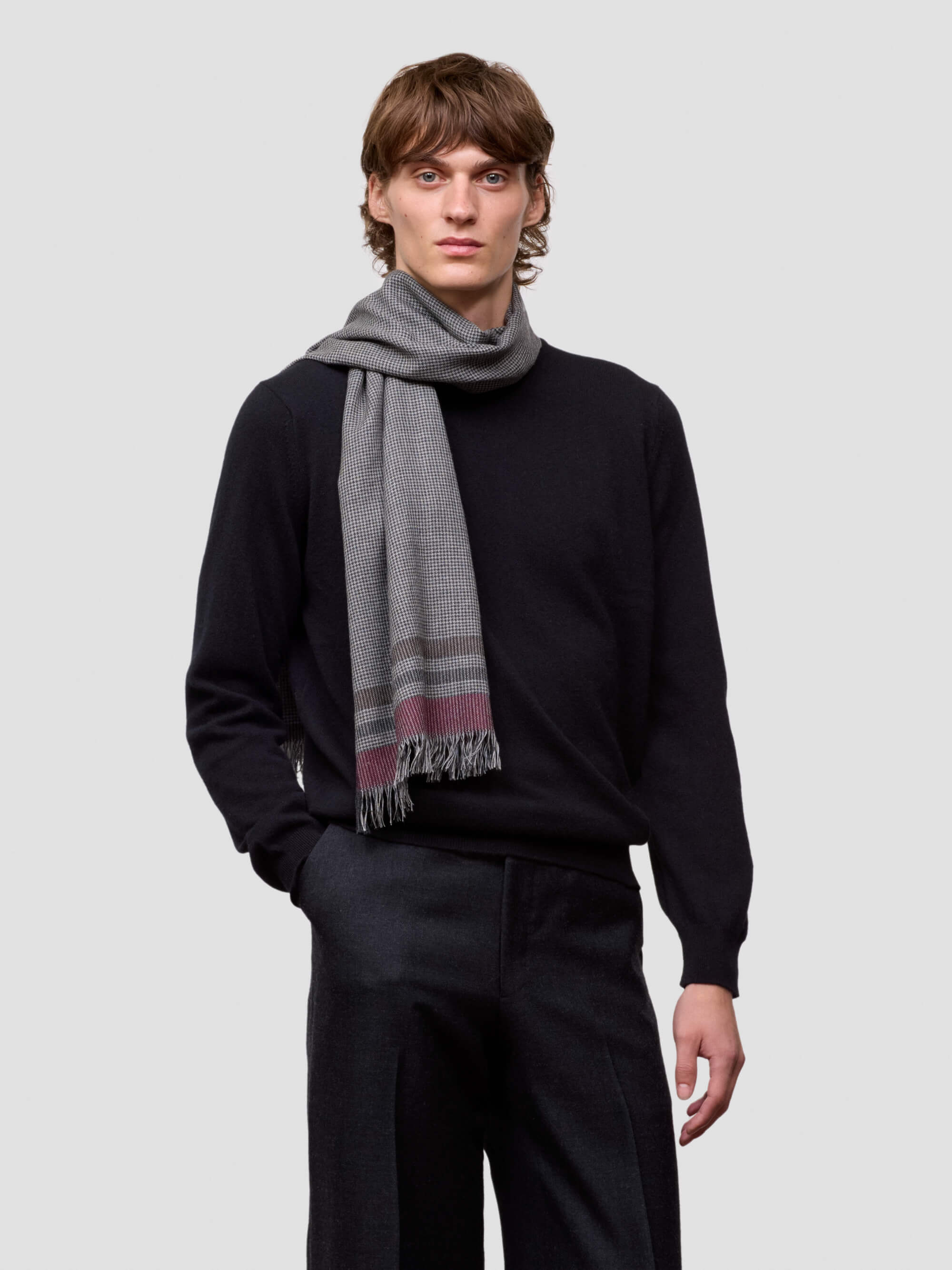 Man wearing a black sweater and gray striped scarf on a light gray background