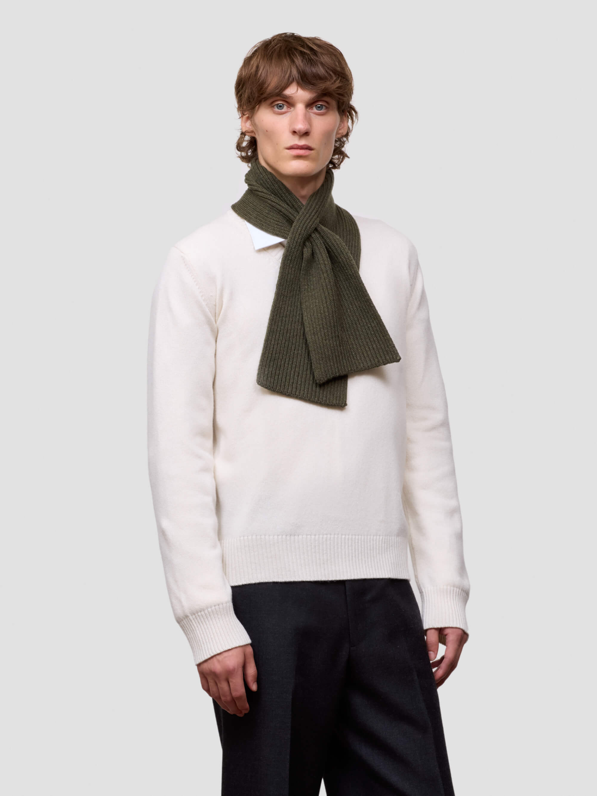 Person wearing a white sweater and dark green scarf on a plain background