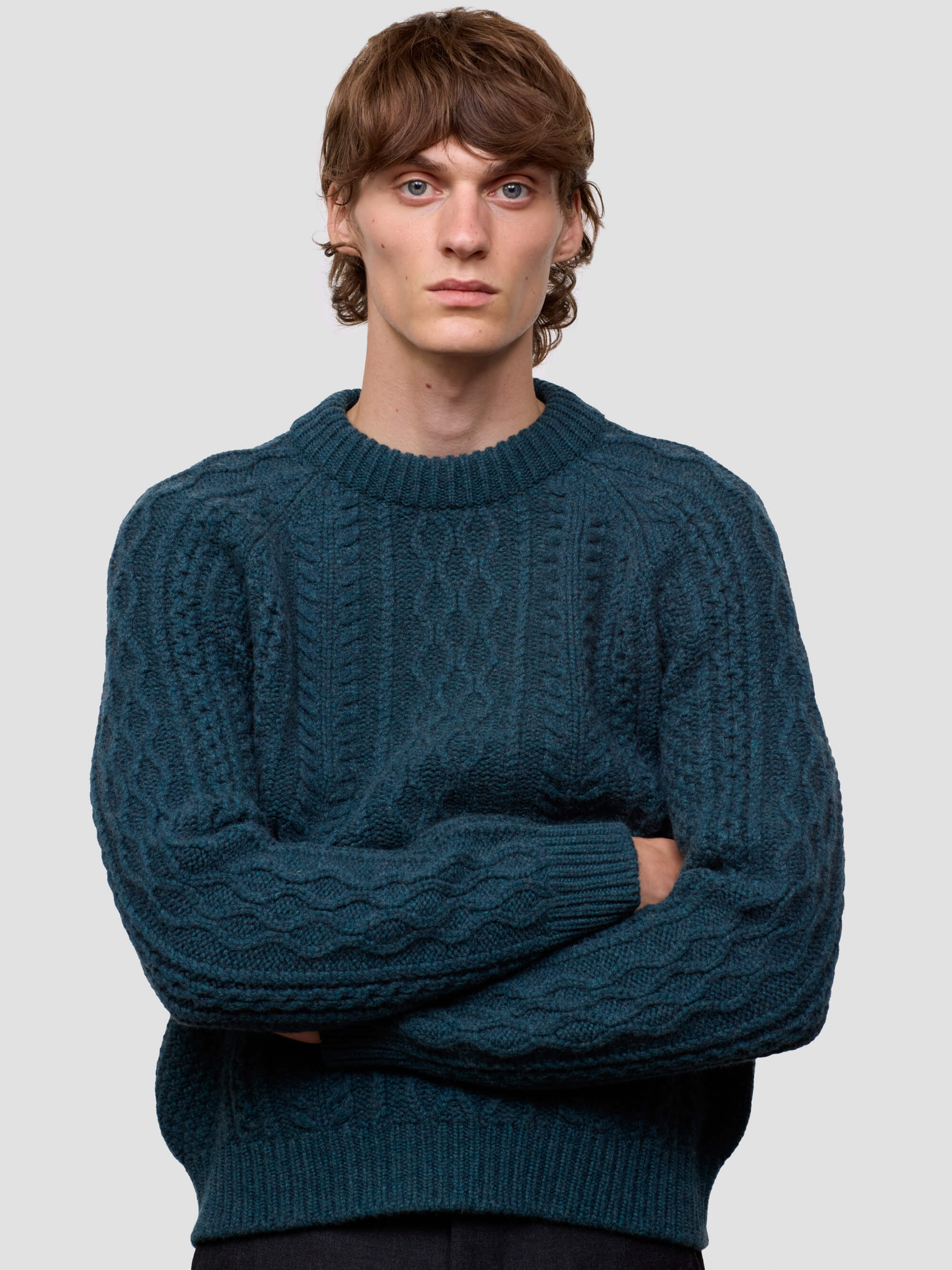 Man wearing a teal cable knit sweater against a plain background