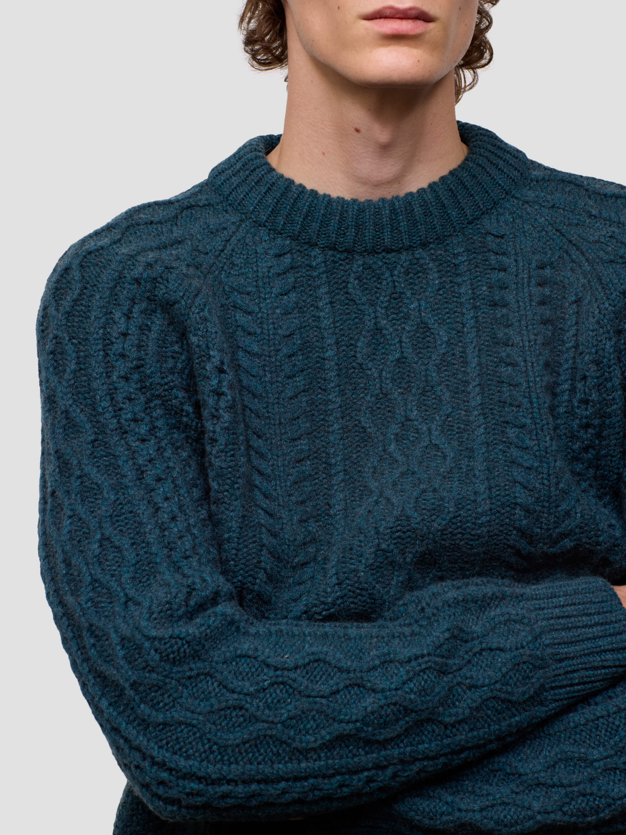 Person wearing a dark green cable knit sweater on a light gray background