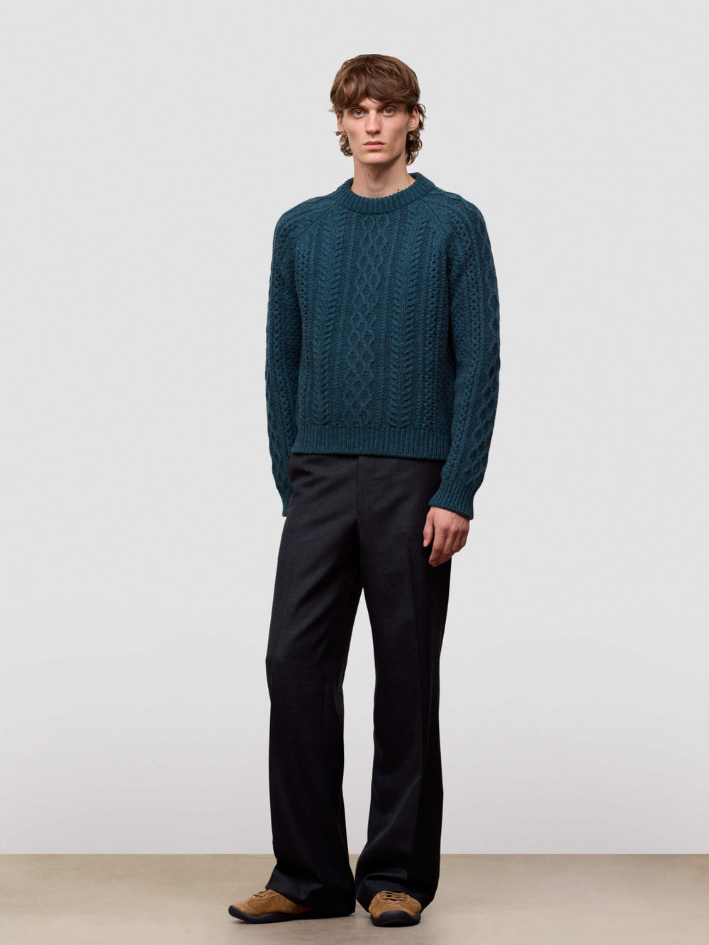 Man wearing a teal sweater and black pants against a white background