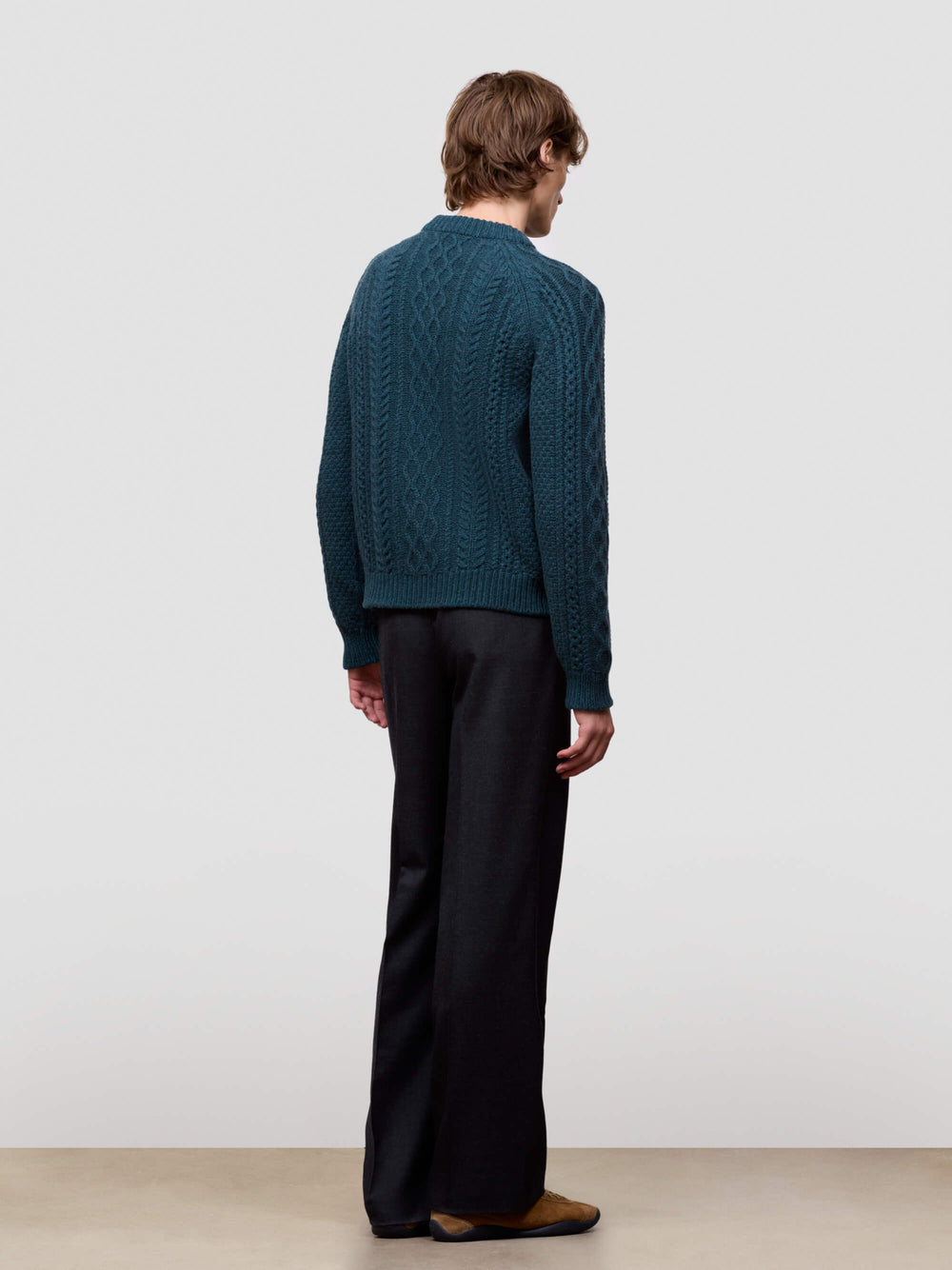 man wearing a teal sweater and black pants on a plain background