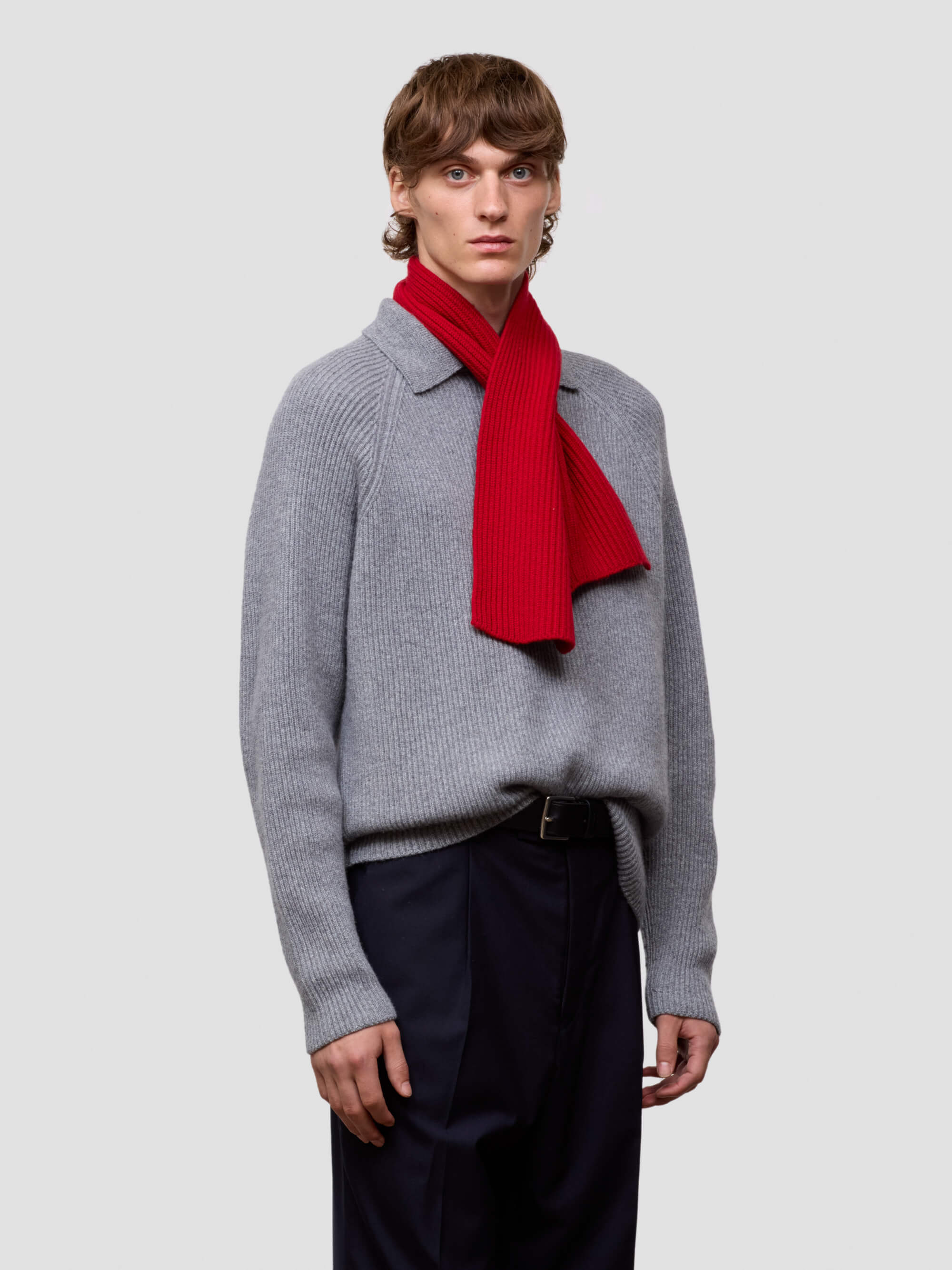 man wearing a ribbed grey zip sweater and red knitted scarf on a white background