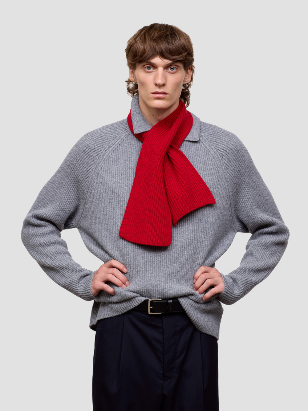 Person wearing a gray sweater with a red scarf on a plain background