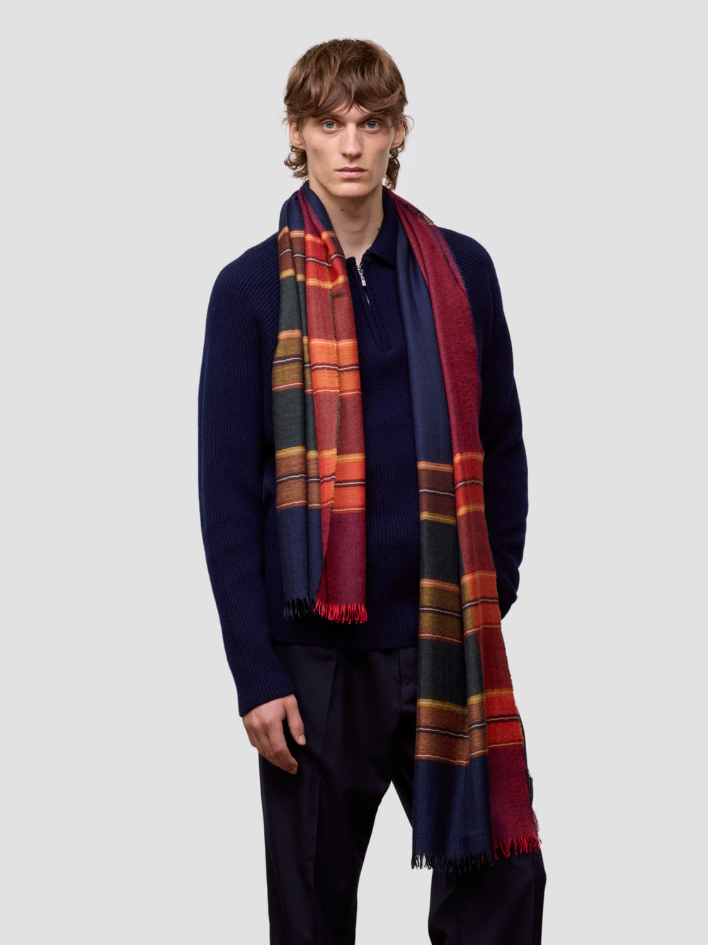 Man wearing a colorful plaid scarf and navy sweater on a light gray background