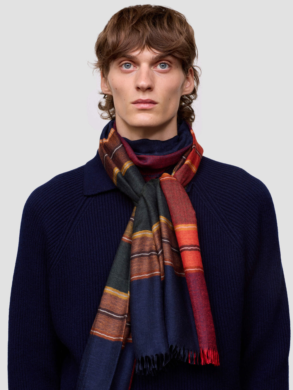 Man wearing a colorful cashmere silk scarf and dark navy sweater against a plain background