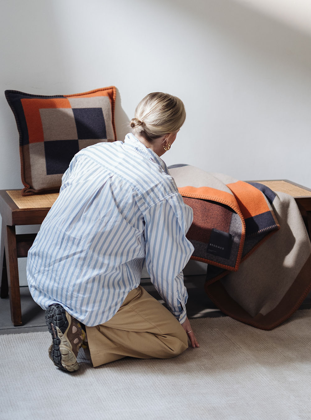 a women adjusting an orange cashmere lambswool throw and cushion on a wooden bench