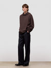 Man wearing a brown sweater and black pants against a plain background