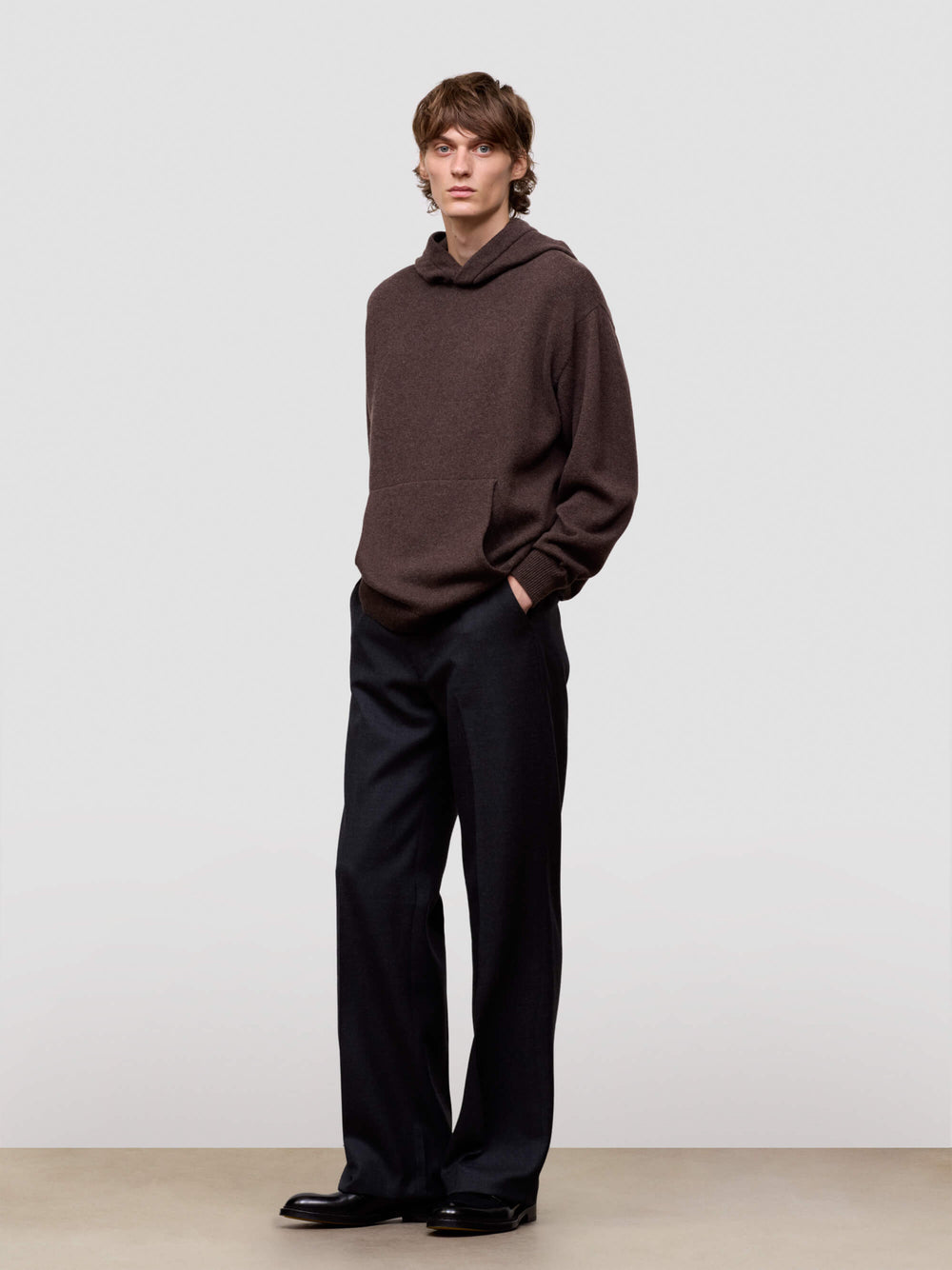 Man wearing a brown sweater and black pants against a plain background
