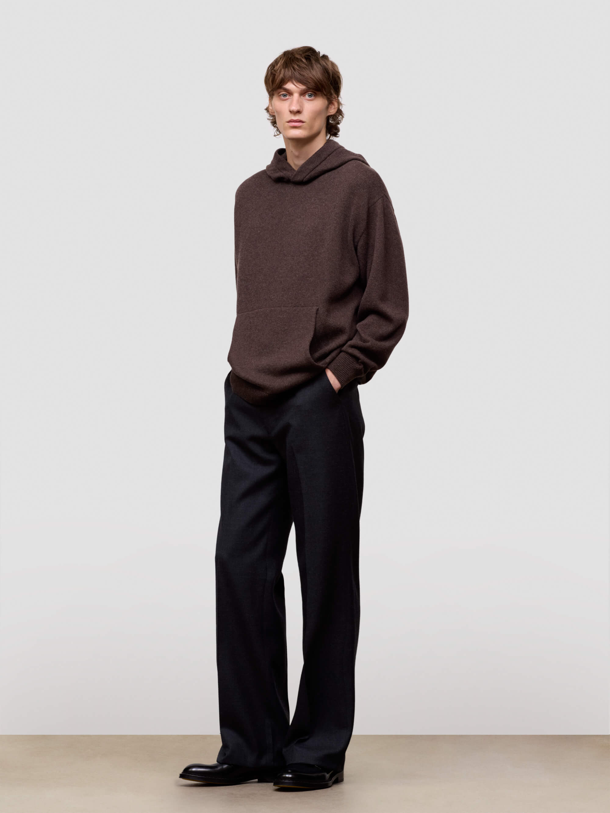 Man wearing a brown sweater and black pants against a plain background