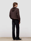 man wearing a brown hoodie and black pants standing against a white background