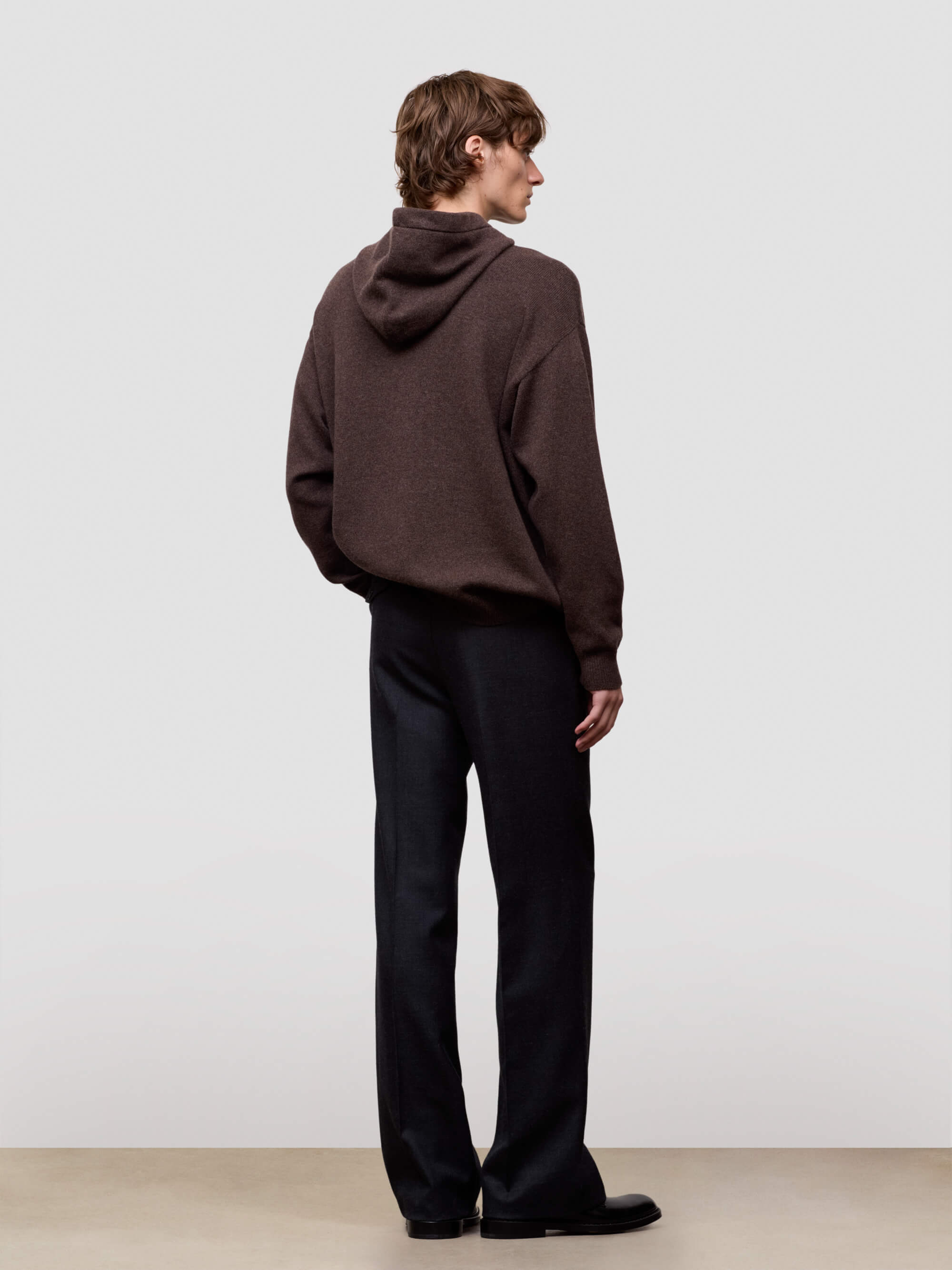man wearing a brown hoodie and black pants standing against a white background