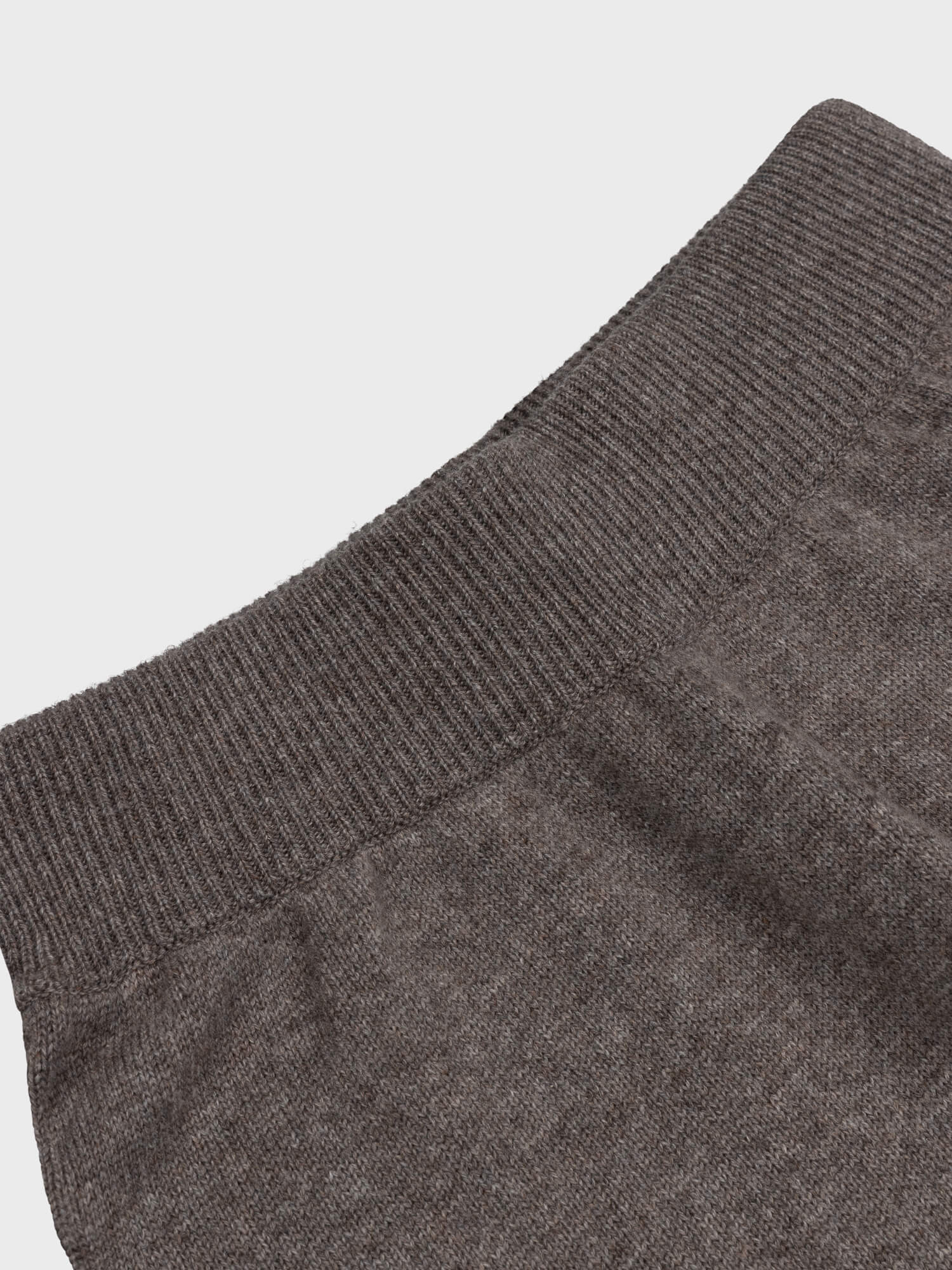 Close-up of a brown cashmere sweatpants with a textured pattern on a light gray background