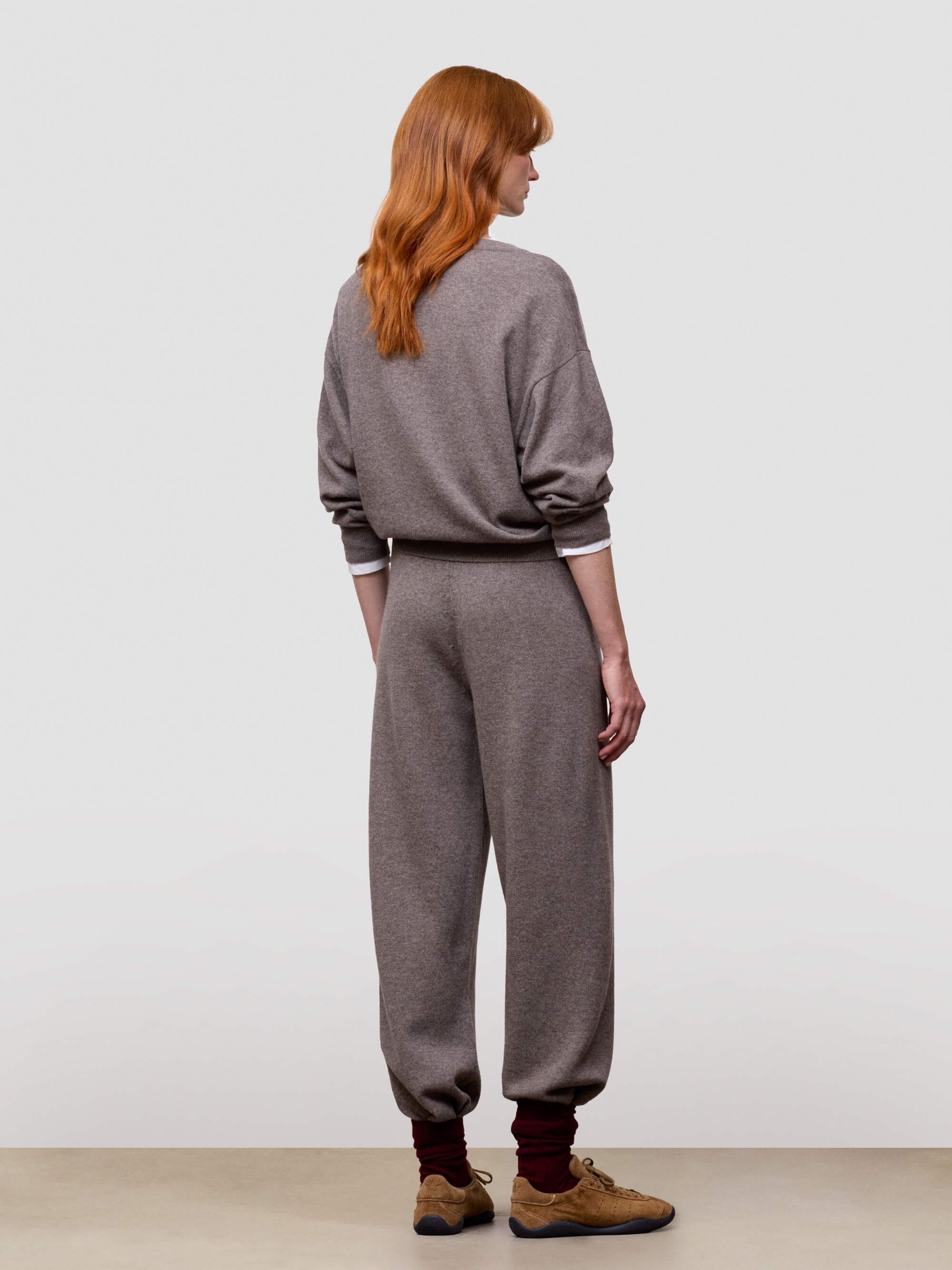 women wearing a brown sweater and pants set with brown shoes on a plain background