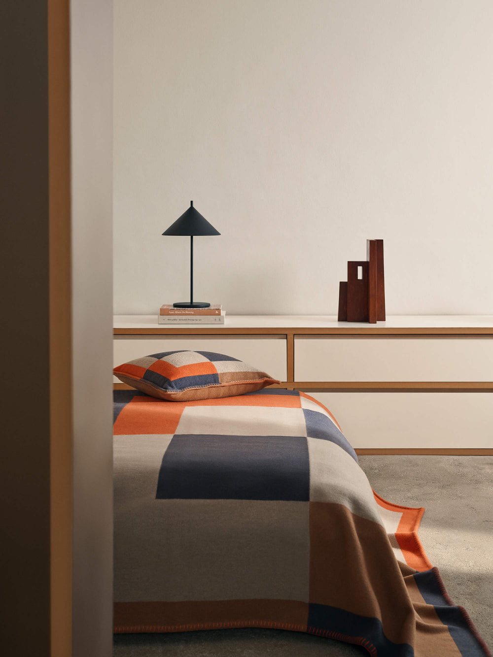Bedroom with a bed covered in a colorful blanket, a lamp, and decorative items on a shelf.