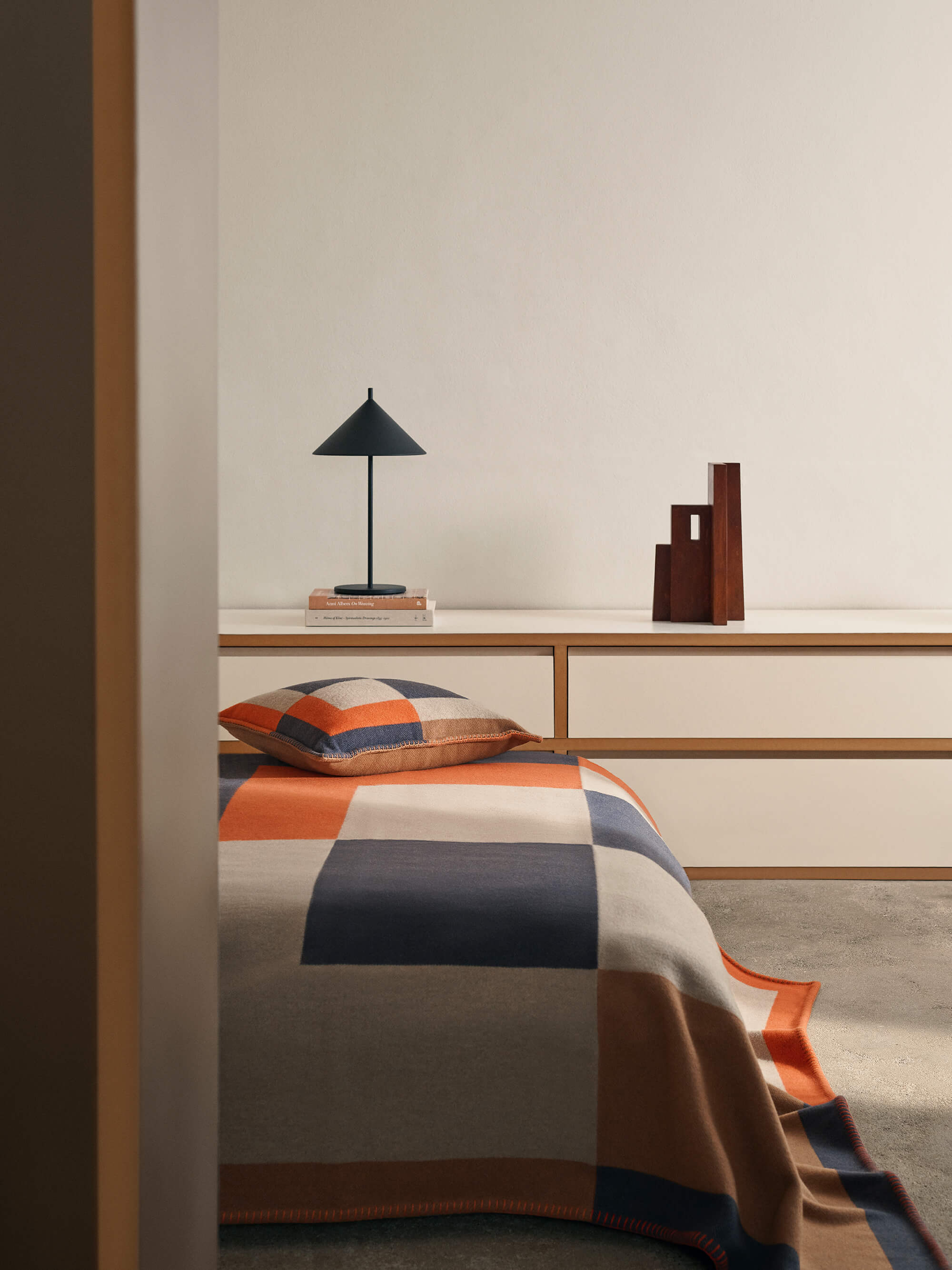 Bedroom with a bed covered in a colorful blanket, a lamp, and decorative items on a shelf.