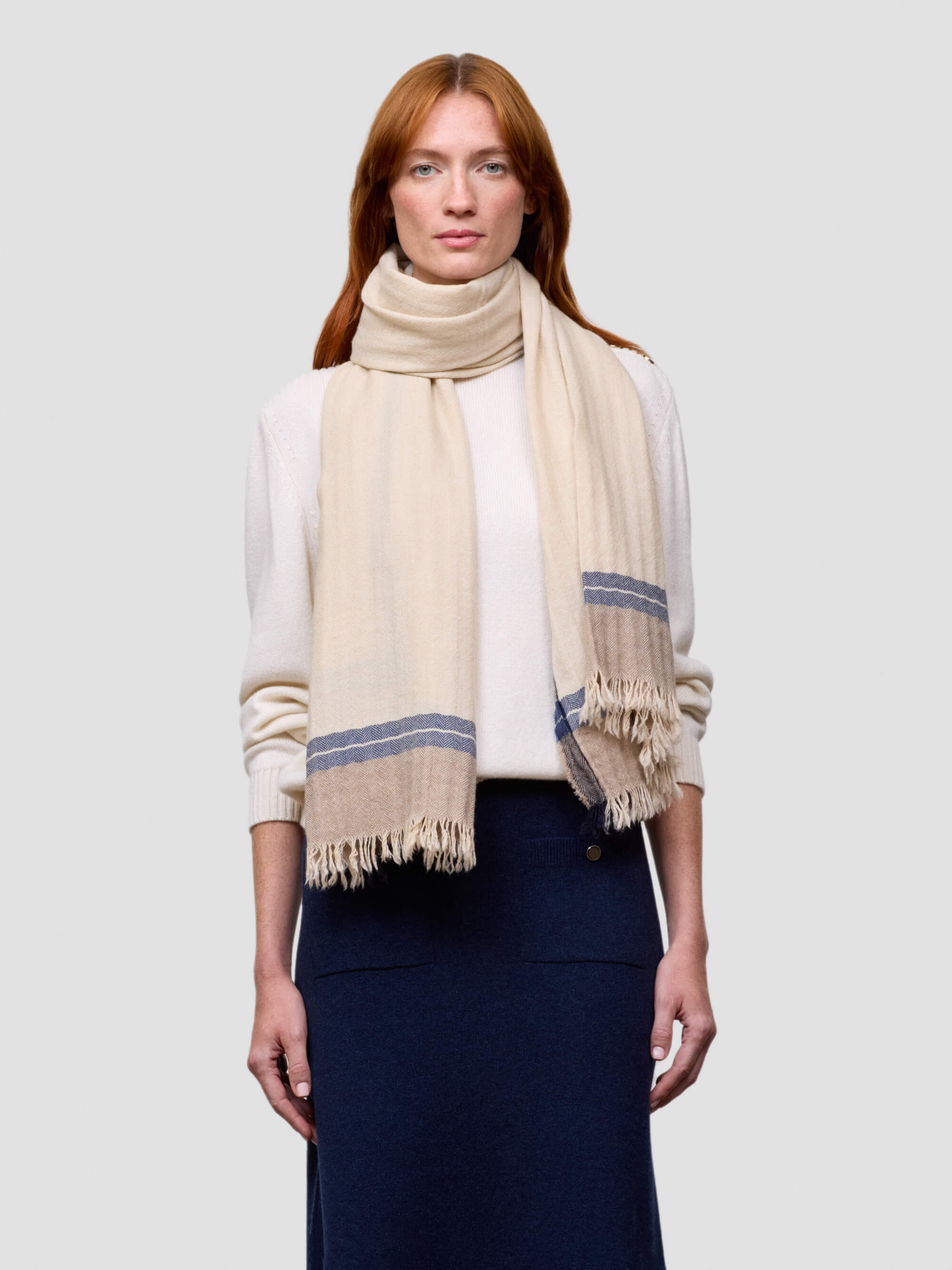 Woman wearing a beige scarf with blue stripes on a plain background