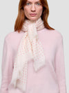 Woman wearing a light pink sweater and a white scarf with red polka dots on a plain background