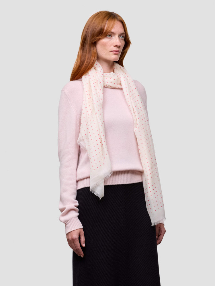 Woman wearing a pink sweater and black skirt with a white polka dot scarf on a light gray background
