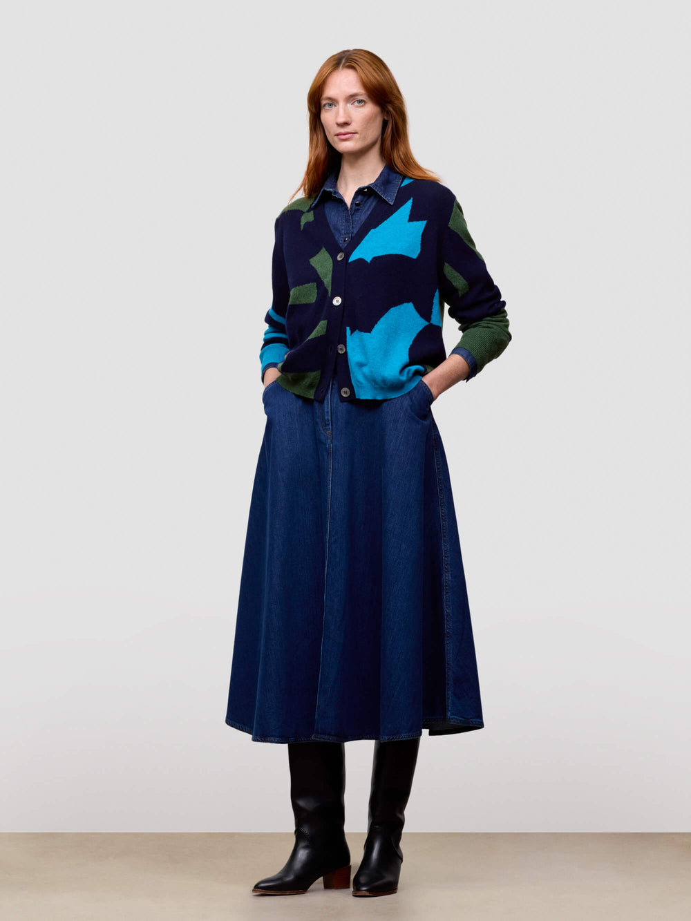 Woman wearing a blue patterned cardigan and dark blue skirt against a white background