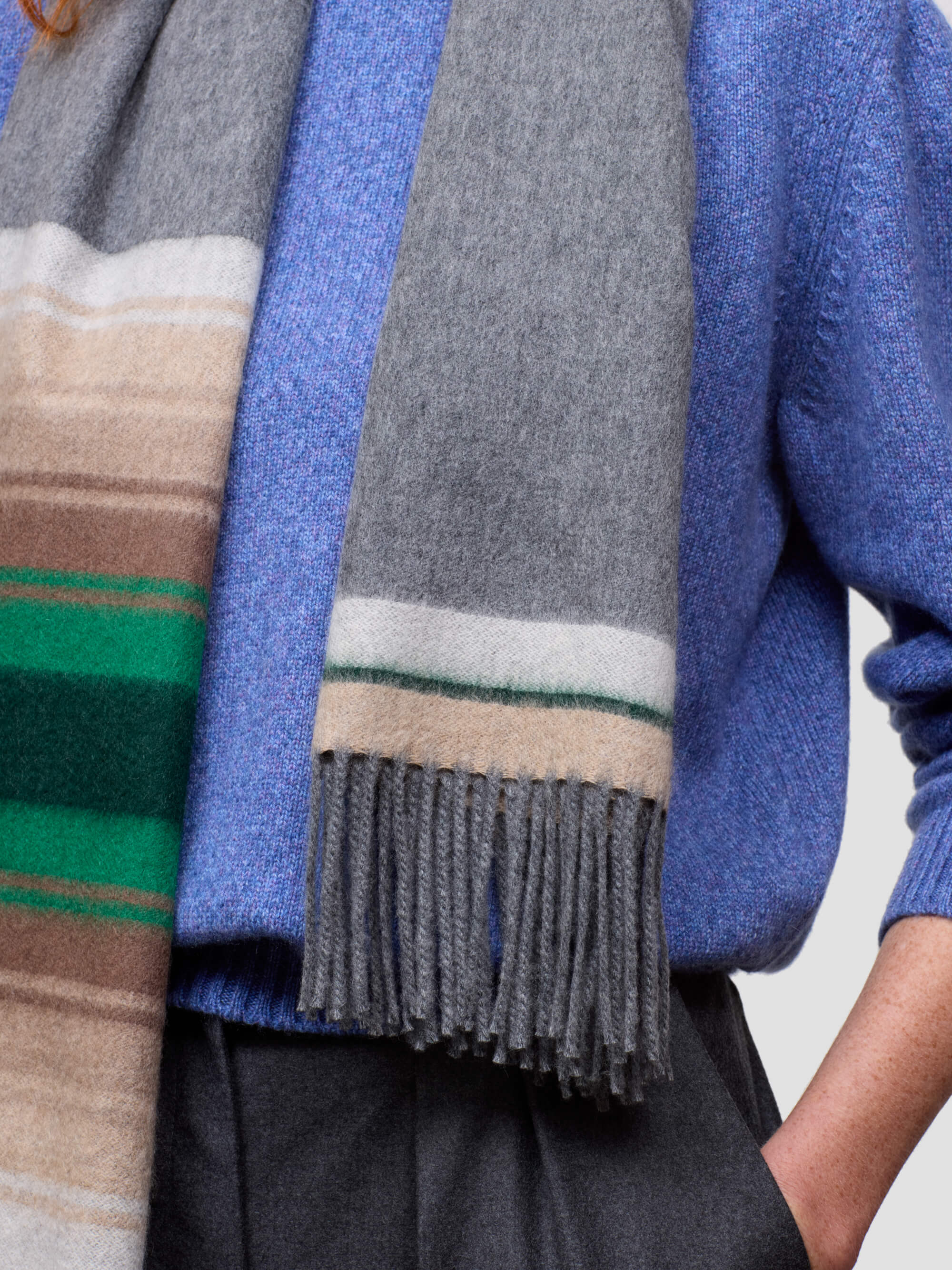 Gray scarf with colorful stripes draped over a blue sweater on a neutral background