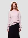 Woman wearing a light pink cashmere  sweater and black skirt on a white background